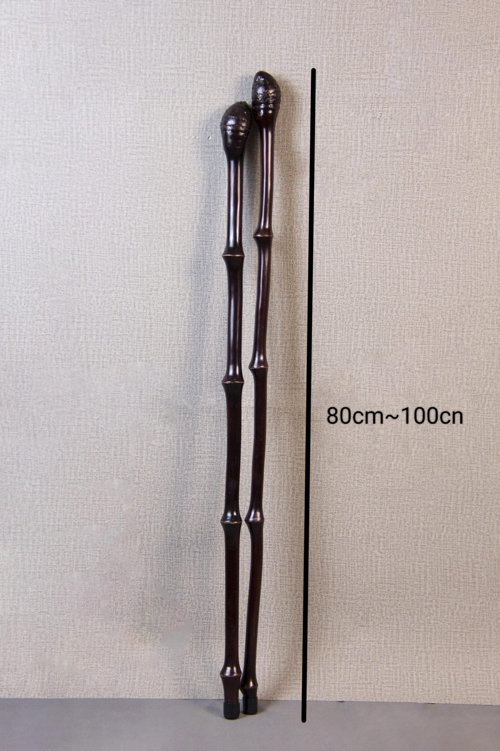 Pair of darkly polished bamboo walking sticks, standing upright with a height range of 80cm to 100cm, showcasing natural joint deformities against a beige textured background.