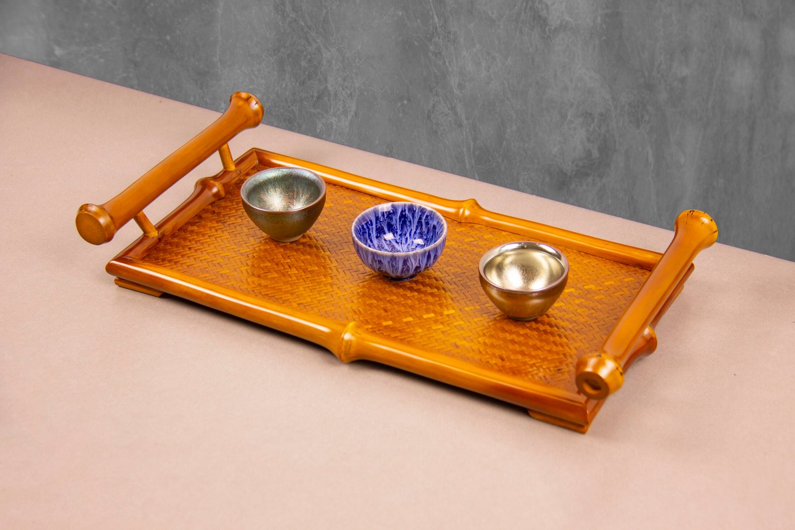 Elegant bamboo serving tray with curved handles featuring three ceramic bowls on a woven bamboo surface.