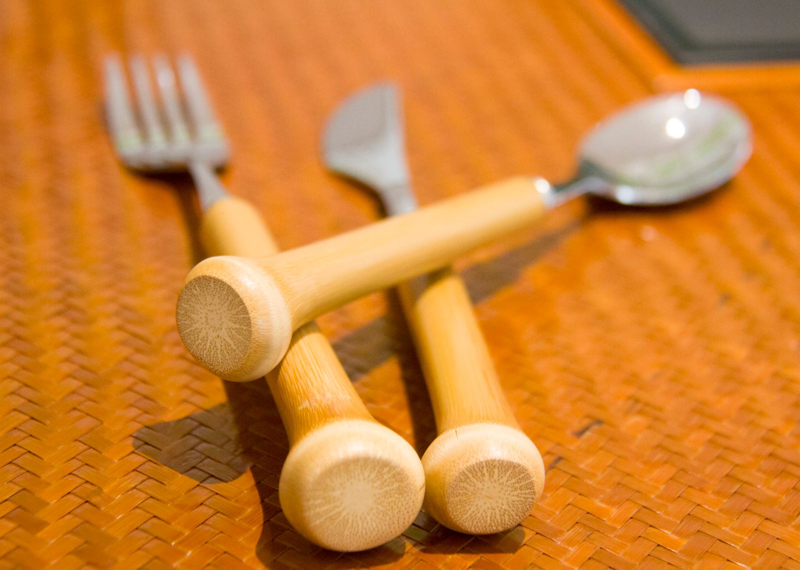 Close-up of eco-friendly bamboo cutlery set including a fork, knife, and spoon with bamboo handles placed on a woven bamboo mat.