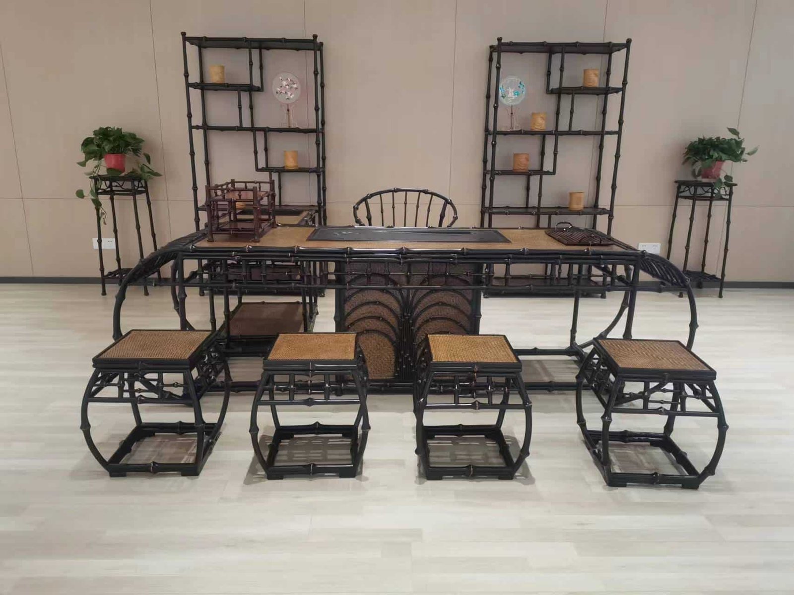 The High-End Antique Chinese Style Qiongzhu Bamboo Living Room Tea Table set includes a central tea table surrounded by six stools, all placed on light wood flooring. Two decorative shelves, adorned with various items and potted plants, frame the set, infusing an antique Chinese style that elevates the room’s aesthetic.