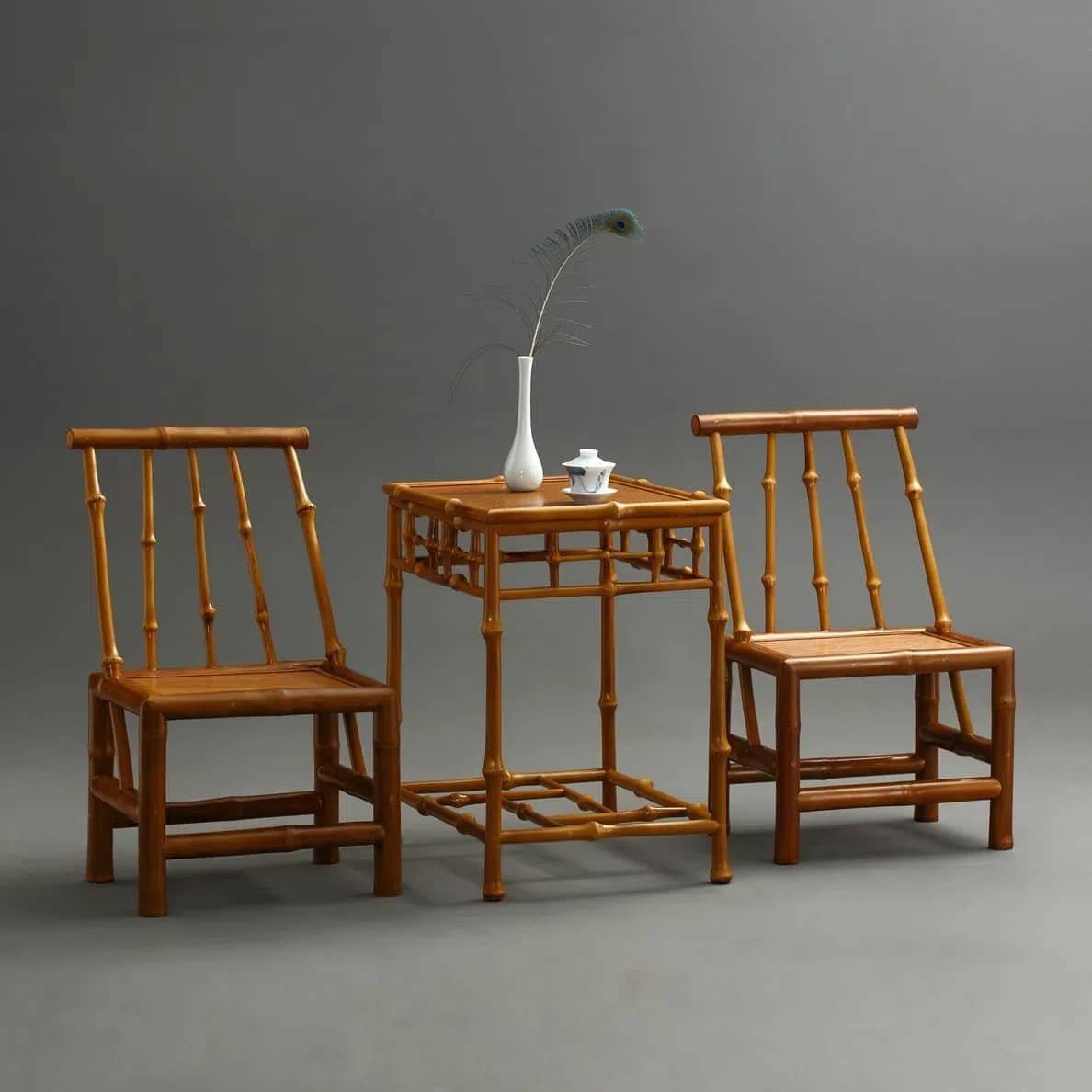 Two Home Use Qiongzhu Bamboo Armless Backrest Small Chairs with Weaving Mats are positioned on either side of a matching table. The table features a white vase holding a single decorative feather and a small ceramic tea set, all placed against a simple gray backdrop.