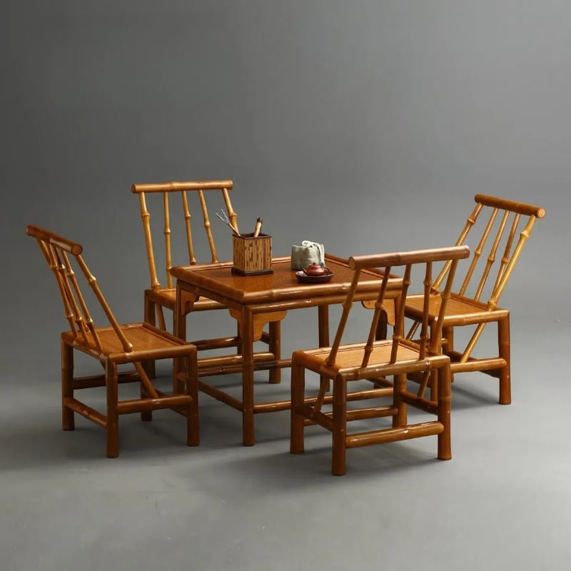 In a simple, empty room, a bamboo dining set featuring the Home Use Qiongzhu Bamboo Armless Backrest Small Chairs with Weaving Mats accompanies a rectangular table. A small basket containing utensils and a teapot on a tray rest on the table, all contrasted against a plain gray background, making it perfect for home use.