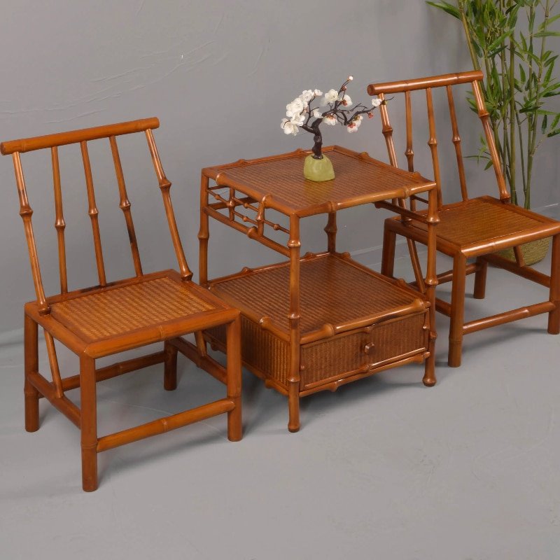 The delightful furniture set features two Home Use Qiongzhu Bamboo Armless Backrest Small Chairs with Weaving Mats and a table, all accented by a vase of white flowers. This setup is showcased on a gray floor, with the verdant Qiongzhu Bamboo adding an elegant backdrop to the scene.