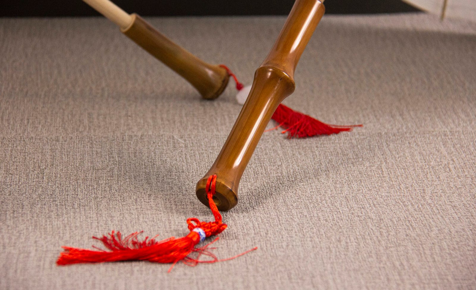 Close-up of the Oil Paper Umbrella - Decorative & Antique Handmade & Waterproof Umbrella, with vibrant red tassels dangling from it, resting on a textured gray surface. The focus is on the intricate details of the umbrella and tassels.