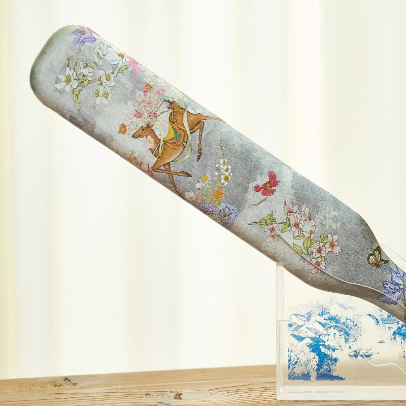 A decorative bat on a wooden stand features colorful floral patterns and a horse and rider illustration. The background is softly lit, highlighting the intricate design.