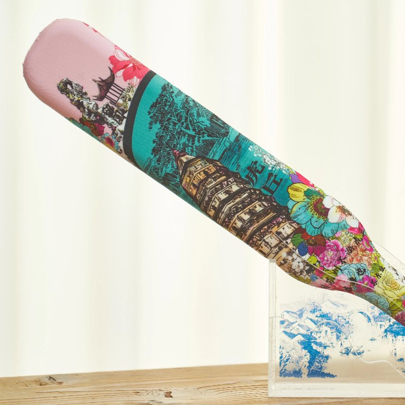 A paddle with vibrant prints of colorful flowers and architectural landmarks, displayed upright against a light-colored background on a wooden surface.