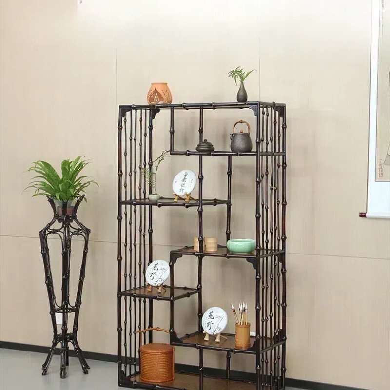 A minimalist bamboo shelf against a beige wall holds decorative items, including teapots, plates, and small plants. Next to it, a potted plant stands on a tall bamboo stand, adding greenery to the scene.
