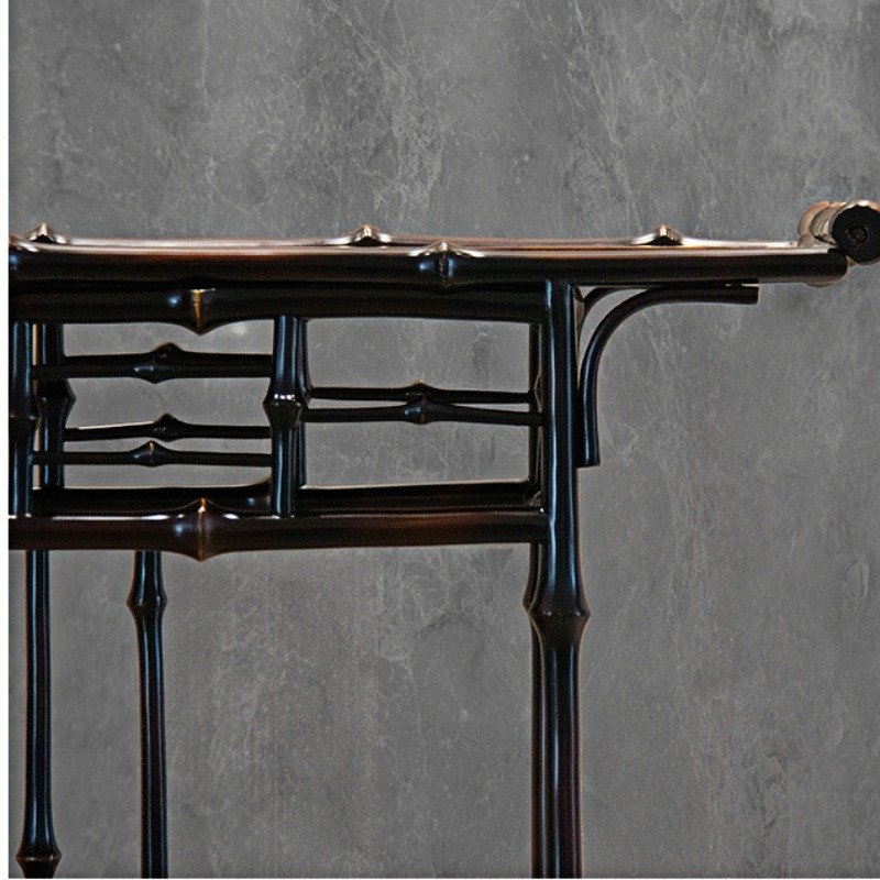 Close-up of a dark, intricately designed wooden table with multiple carved layers and decorative features set against a textured gray wall.