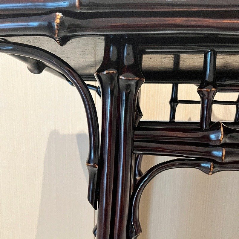 Close-up of a dark wooden table with bamboo-inspired legs and intricate detailing. The reflection and shadows highlight the glossy finish and unique design.